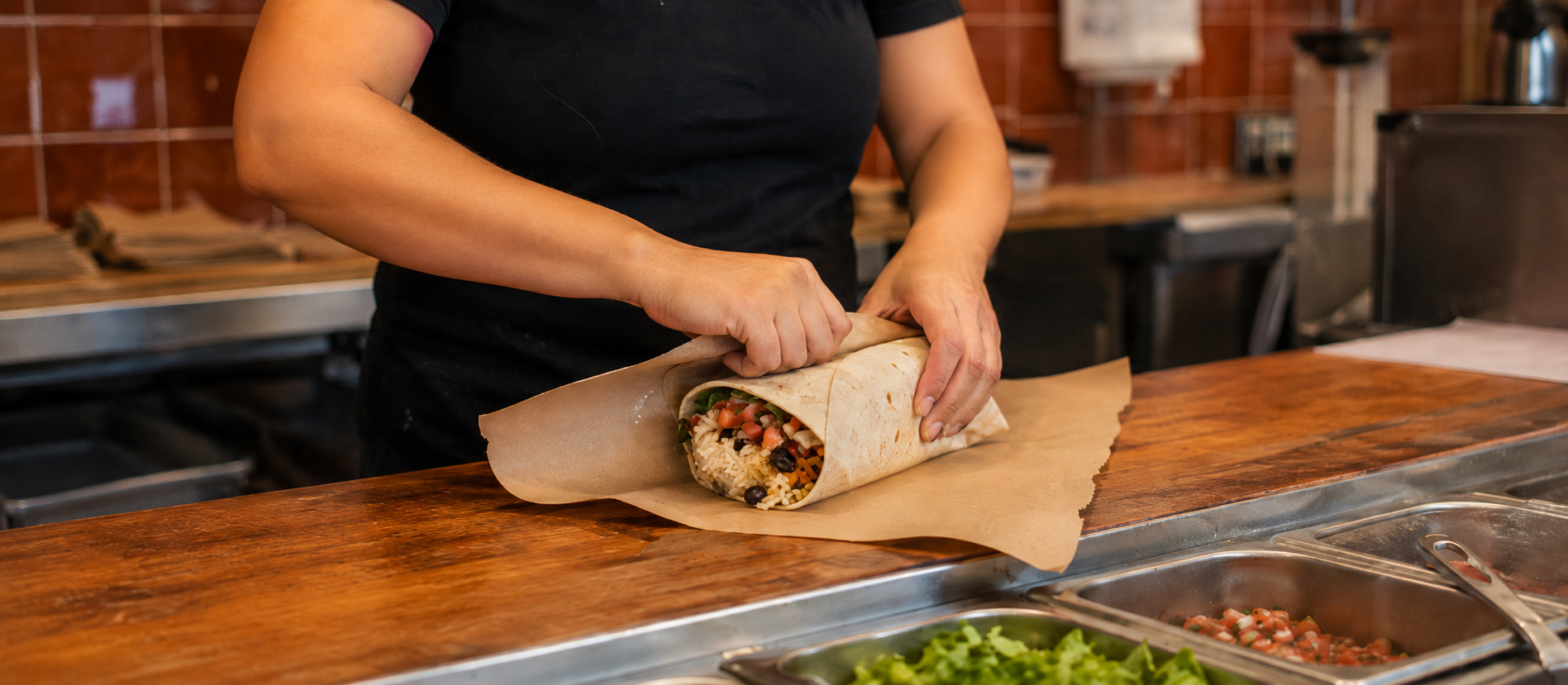 Manos envolviendo un burrito recién armado en el mostrador